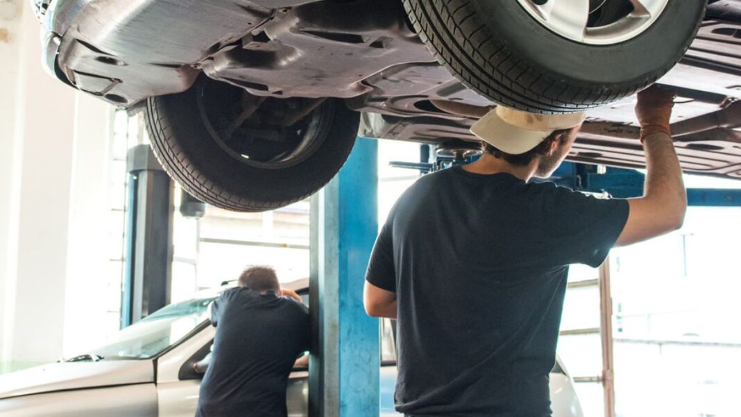 Mecánico trabajando bajo un vehículo elevado en un taller de reparación de automóviles.